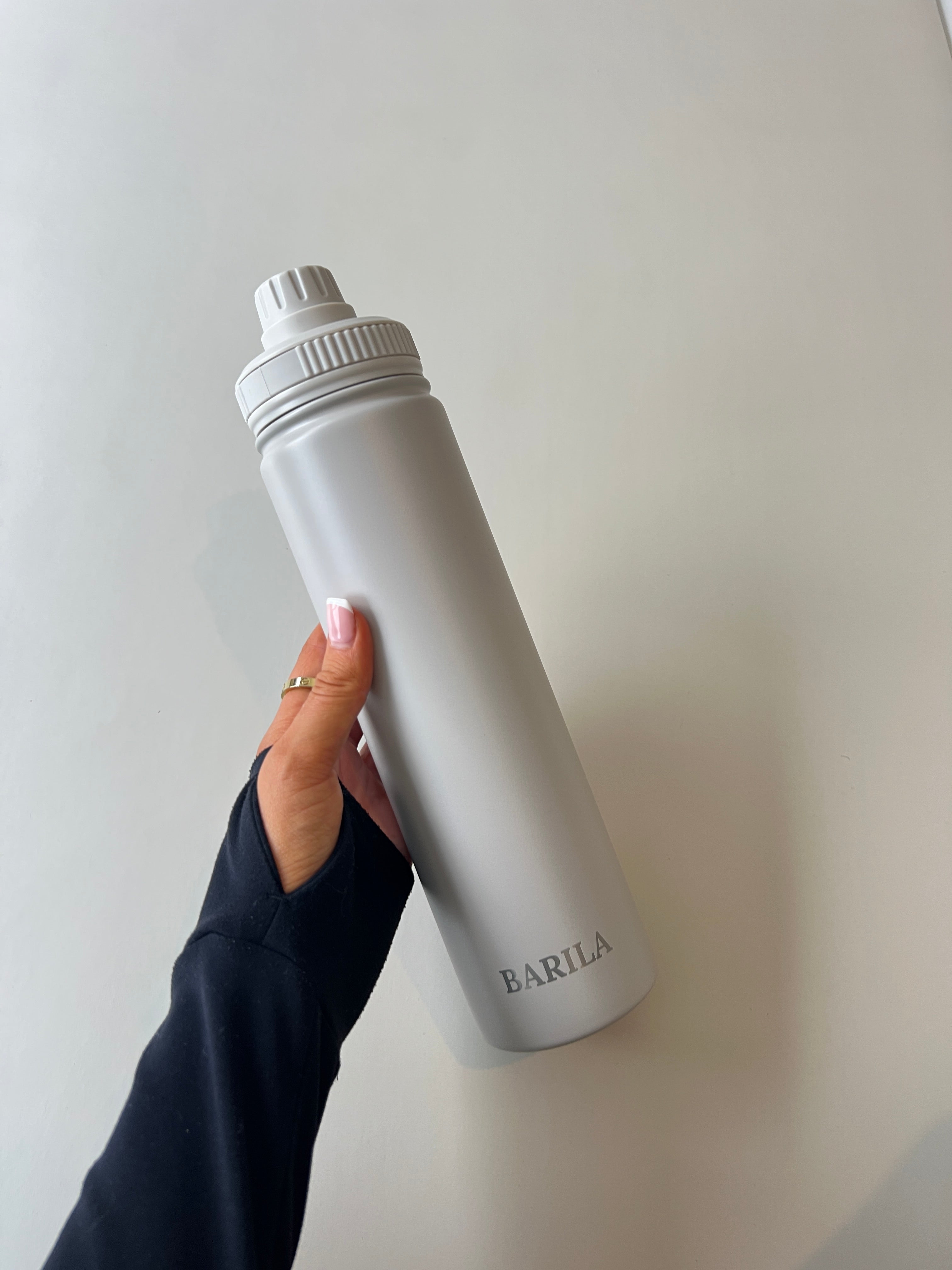 Person holding a beige steel water bottle with 'Barila' branding against a light background